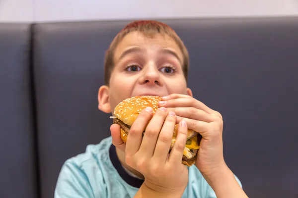 Rapaz bonito está comendo hambúrguer — Fotografia de Stock