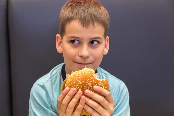 Rapaz bonito está comendo hambúrguer — Fotografia de Stock