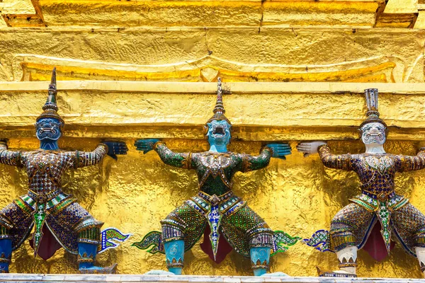 Demon Guardian Statues are supporting golden Chedi stupa at Wat Phra Kaew temple in a sunny day