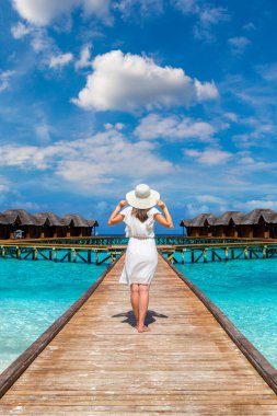 Maldivler adasındaki tropikal sahil iskelesinde (ahşap iskele) duran su lüks villalarının önünde duran güzel genç bir kadın.