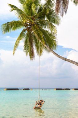 Güzel bir kadın güneşli bir yaz gününde lüks bir tropikal plajda hamakta oturuyor.