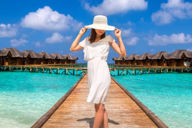 Maldivler adasındaki tropikal sahil iskelesinde (ahşap iskele) duran su lüks villalarının önünde duran güzel genç bir kadın.