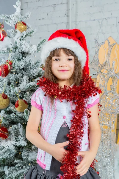 Menina feliz no chapéu do Papai Noel na frente da árvore de Natal — Fotografia de Stock