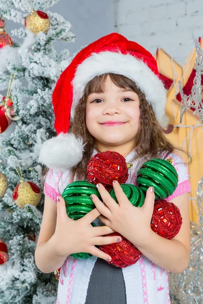 Kleines Mädchen mit Weihnachtsmütze hält Weihnachtsdekoration in den Händen — Stockfoto