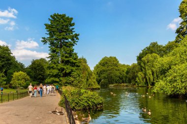 LONDON, İngiltere - 25 Haziran 2024: İnsanlar yaz aylarında St James Park, Londra, İngiltere, İngiltere 'de göl kenarında ördek ve kazlarla yürüyorlar