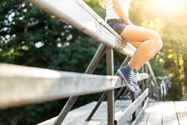 Kot pantolon spor ayakkabıları bir köprü korkuluk üzerinde oturan genç kadın — Stok fotoğraf