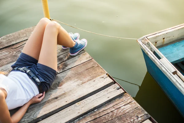 Vrouw in sneakers op een pier op het water — Stockfoto