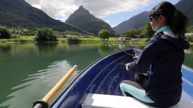 Teknedeki kadın Norveç 'te dönerken balık yakalar. Norveç 'te balık tutmak yerel yaşam tarzını benimsemenin bir yoludur. Sayısız göl ve nehirler ve geniş bir kıyı şeridi olağanüstü fırsatlar demektir.