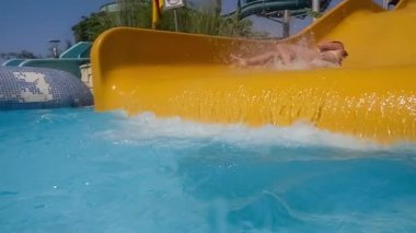Tatil parkındaki su kaydırağından indim. Su kaydırağı aile tatilinde yavaş çekim, bikinili bir kadın mavi su damlalarından oluşan bir havuza iniyor..