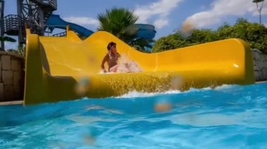 Tatil parkındaki su kaydırağından indim. Su kaydırağı aile tatilinde yavaş çekim, bikinili bir kadın mavi su damlalarından oluşan bir havuza iniyor..