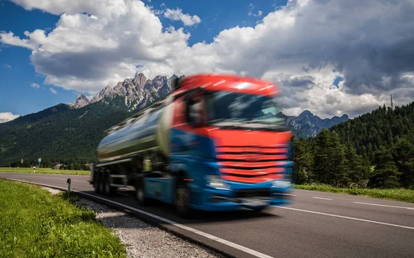燃料トラックはアルプスを背景に高速道路を駆け下ります トラックの車の動きにぼかし ストック画像
