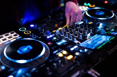 Professional DJ hand adjusting mixer controls at nightclub party