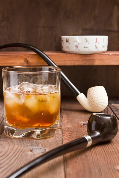 Tobacco pipe and whiskey with ice — Stock Photo, Image