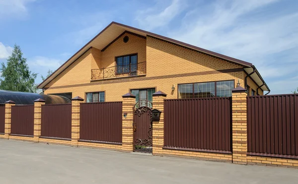 Large yellow brick cottage with brown metal fence — Stock Photo, Image