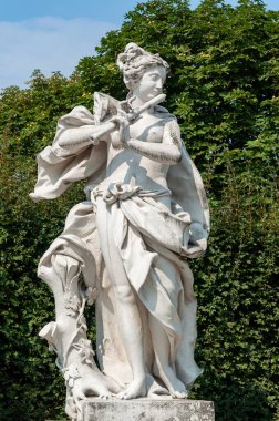 Female sculpture with flute in Lower Belvedere garden on green trees background, Vienna, Austria
