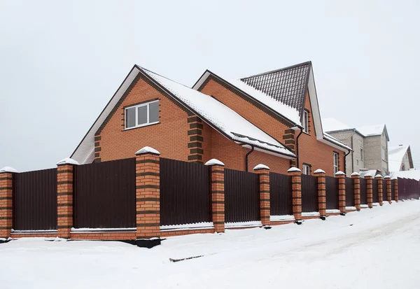 Casa de ladrillo rojo cubierto de nieve con valla de metal — Foto de Stock