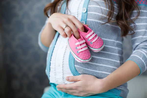 Happy future mother with pink booties in hand