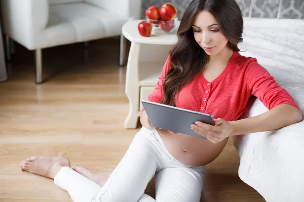 Vakker, gravid kvinne med nettbrett i hånden – stockfoto