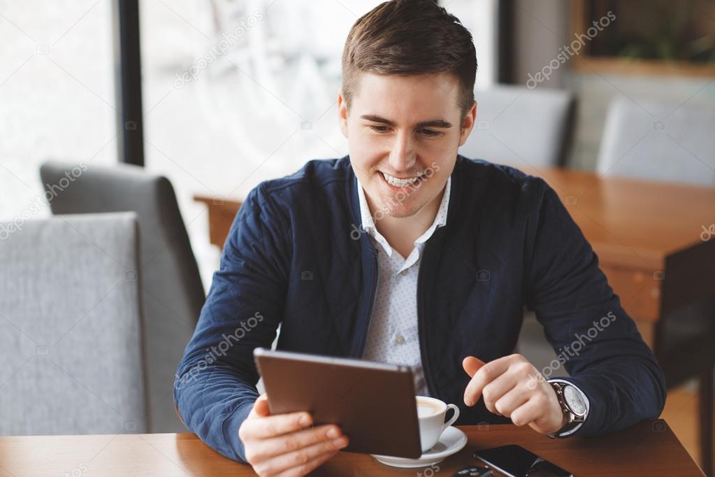 Handsome Man Drinking Coffee And Using Tablet Computer Inside Cafe Bar.
