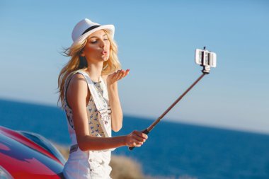 Woman making selfie portrait near the car by the sea.