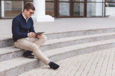 Business man with tablet computer sitting on stairs near business center.