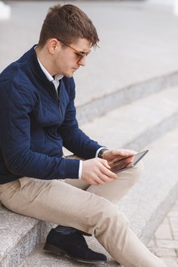 Business man with tablet computer sitting on stairs near business center.