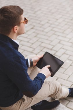 Business man with tablet computer sitting on stairs near business center.
