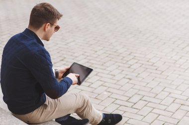 Business man with tablet computer sitting on stairs near business center.