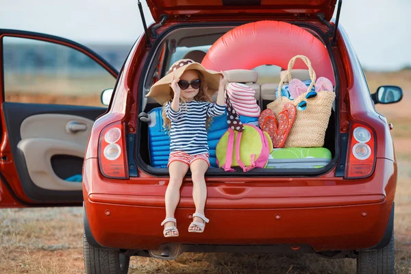 Bambina in cappello di paglia seduta nel bagagliaio di una macchina — Foto Stock