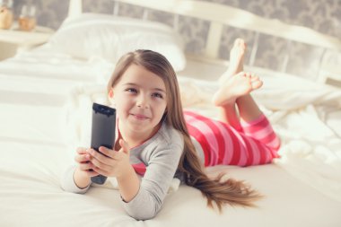 Küçük kız bir uzaktan kumanda Tv ile yatakta yatan