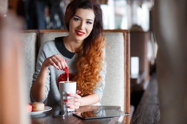 Kafede bir fincan kahve içen kızıl saçlı bir kadın.