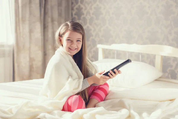 Petite fille couchée au lit avec une télécommande TV — Photo