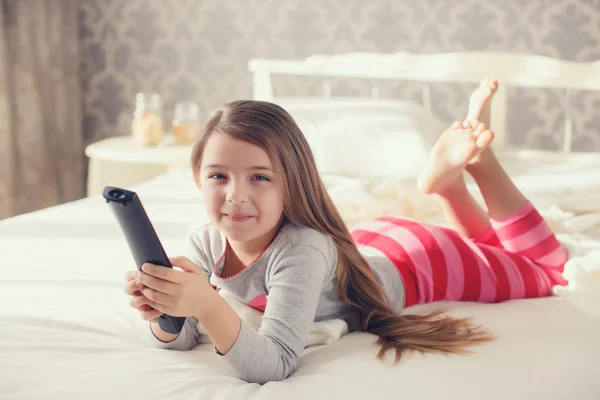 Niña acostada en la cama con un televisor de control remoto —  Fotos de Stock