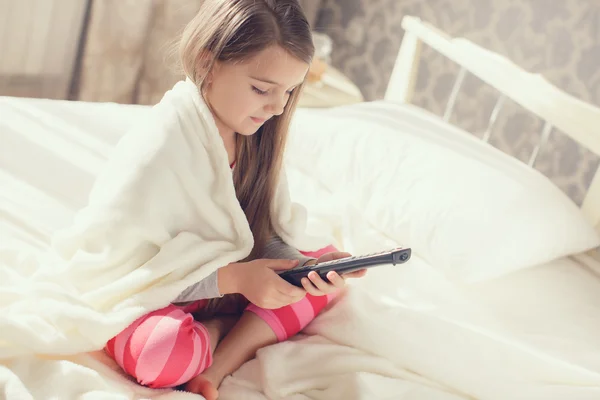 Маленькая девочка лежит в постели с телевизором с дистанционным управлением — стоковое фото