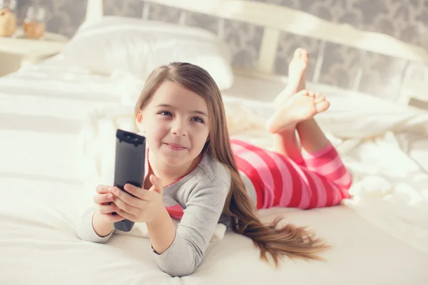 Маленькая девочка лежит в постели с телевизором с дистанционным управлением — стоковое фото