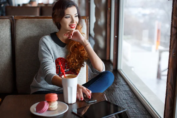 En rödhårig kvinna med en kopp kaffe i caféet — Stockfoto