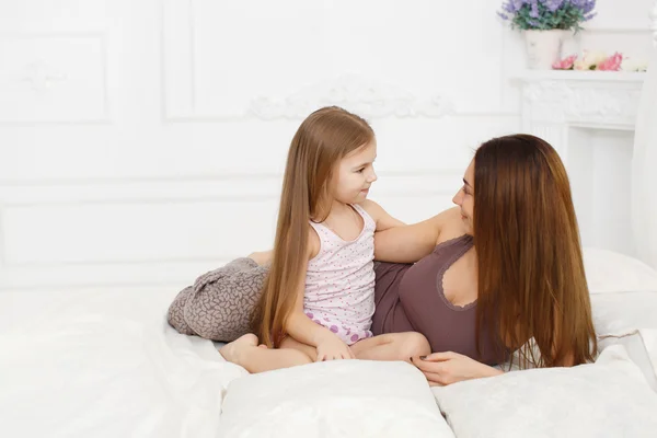 Mother and daughter lying on a white bed in the bedroom — Stok fotoğraf