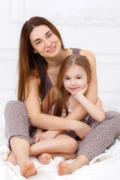 The girl and her mother sitting on a white bed in the bedroom — Stok fotoğraf