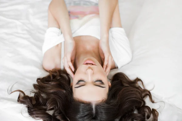 Happy young woman wakes up in a white bed in the morning — Stock fotografie