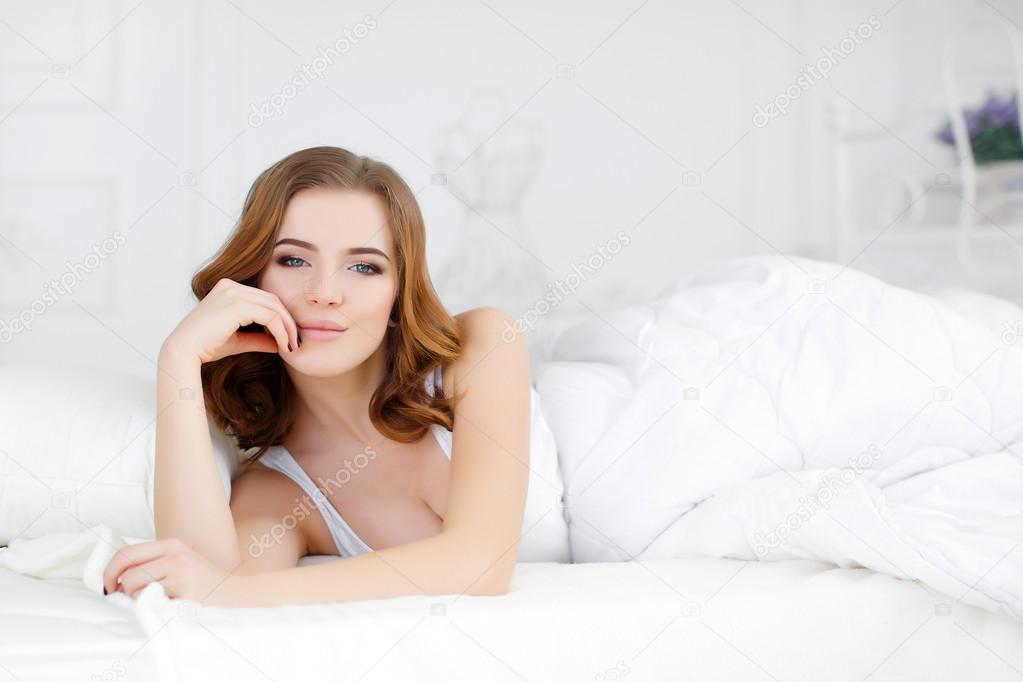 Beautiful girl wakes up in a white bed in the morning