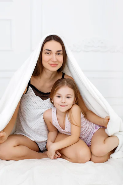 Мать с дочерью играют на кровати, под простынями — стоковое фото