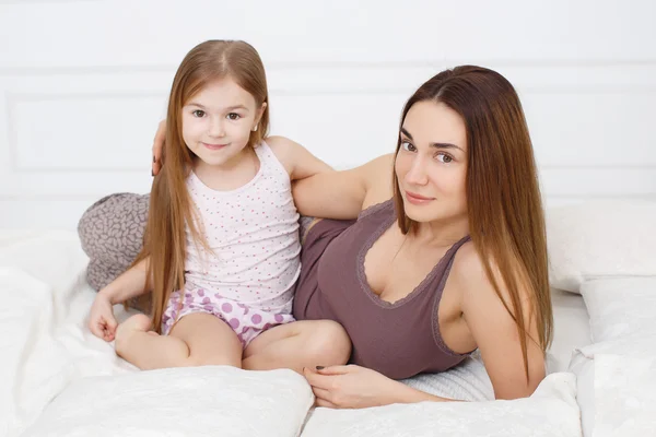 Mother and daughter lying on a white bed in the bedroom — Stock Photo, Image