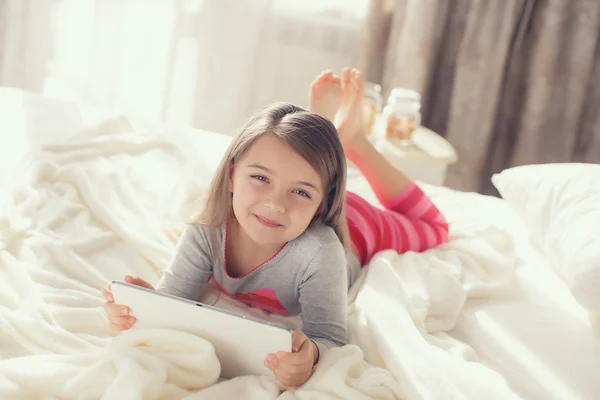 Schattig klein meisje werken met Tablet computer liggend in bed — Stockfoto