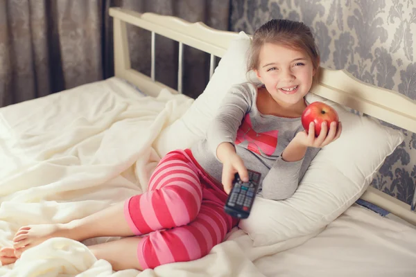 Menina deitada na cama com uma TV de controle remoto — Fotografia de Stock