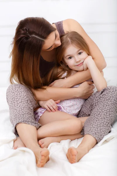 The girl and her mother sitting on a white bed in the bedroom — Stock fotografie