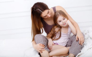 The girl and her mother sitting on a white bed in the bedroom