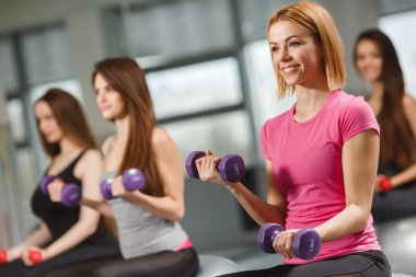 Spor salonundaki kızlar dambıllarıyla egzersiz yapıyor.