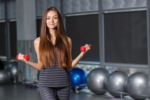 Smiling sporty woman in gym exercising with dumbbells — Stock Photo, Image