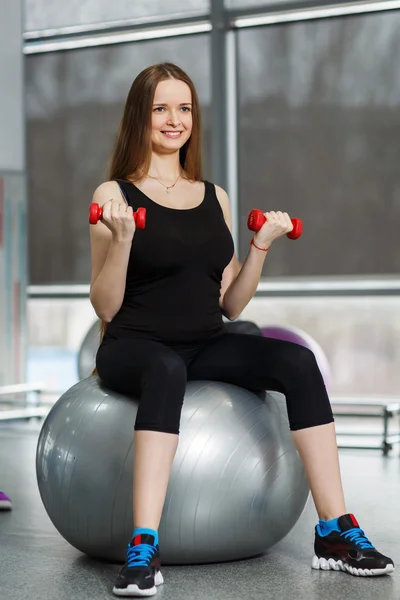 Smiling sporty woman in gym exercising with dumbbells — Stock Photo, Image