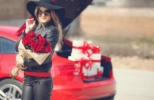 Stylowe blondynka z bukietem czerwonych róż w pobliżu samochodu — Zdjęcie stockowe